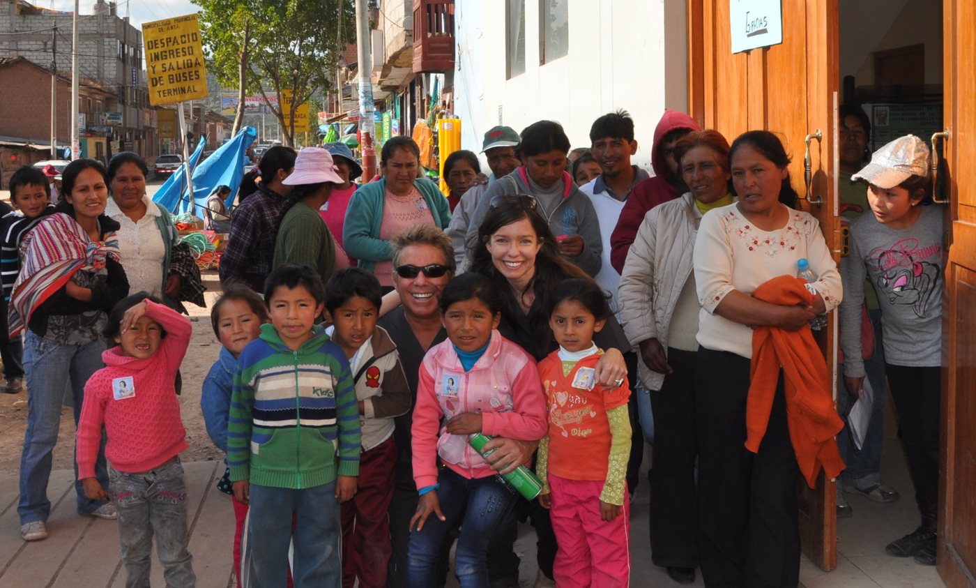 Steve Bender and a volunteer crouch with children and families outside the clinic doors in Anta, Peru