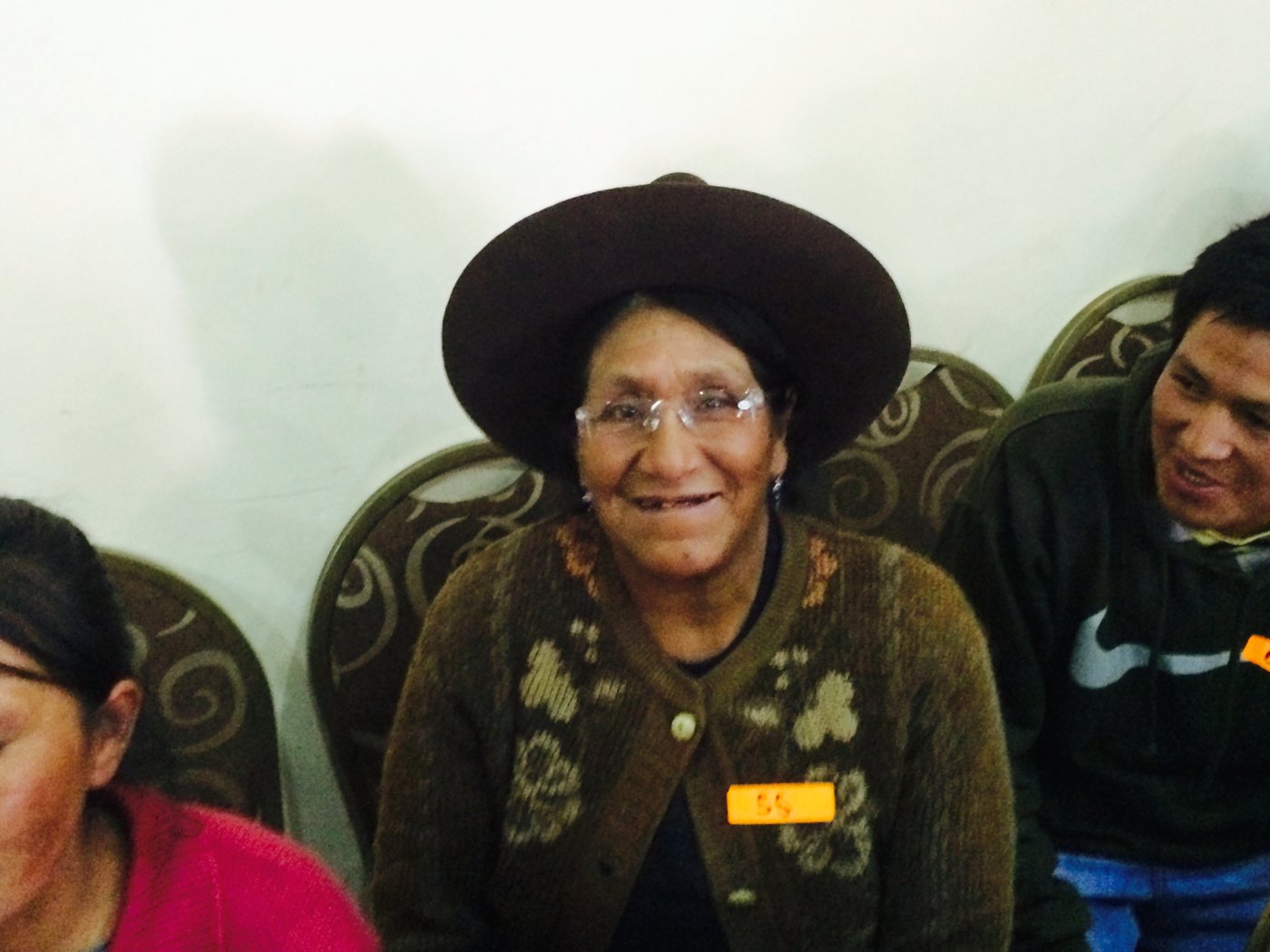 An elderly woman in a brown hat and cardigan grins in her new clear reading glasses at the clinic