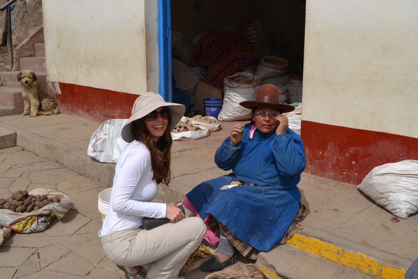 A volunteer in a sun hat crouches beside the potato seller as she adjusts her new glasses